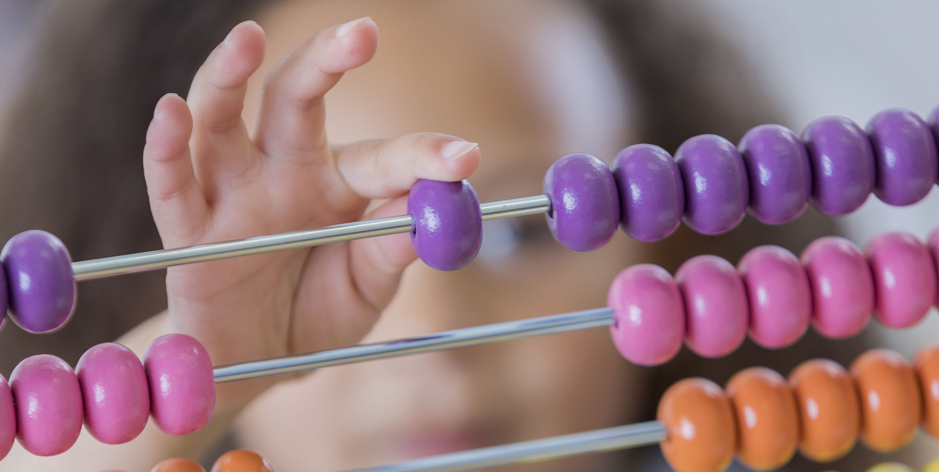 Little girl uses an abacus at school. Focus is on the abacus.