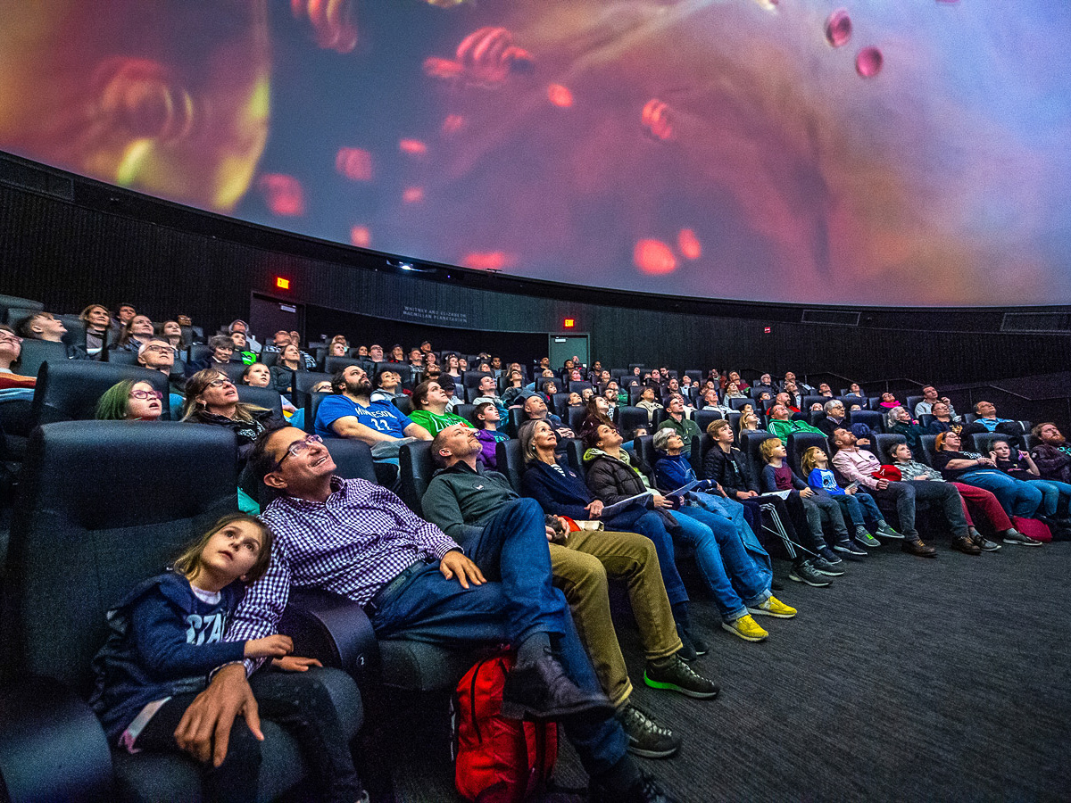 A full audience enjoys colorful scenes inside a planetarium