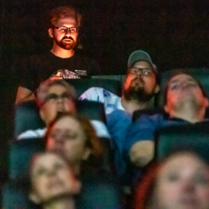 Lit up face of planetarium staff member behind an audience