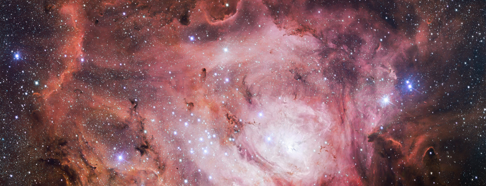 A complex and mesmerizing pink nebula with wisps of red among the stars