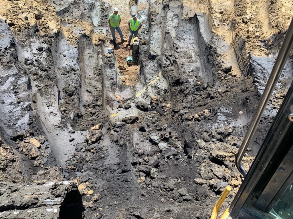 Two people in bright yellow construction gear standing in a 18ft deep hole