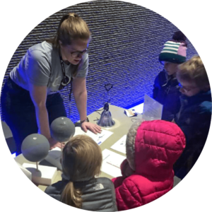 Adult showcasing items to 4 young visitors