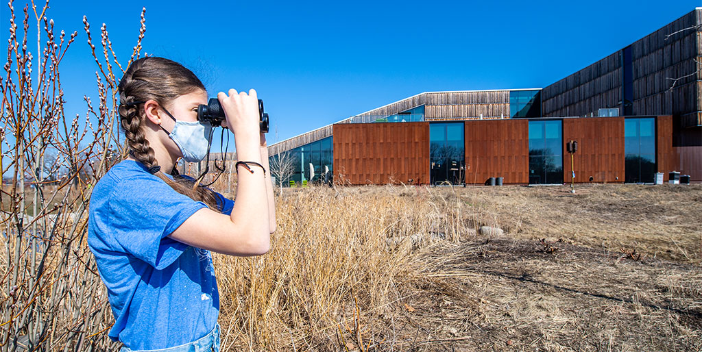 Young adult uses binoculars outside the Bell Museum
