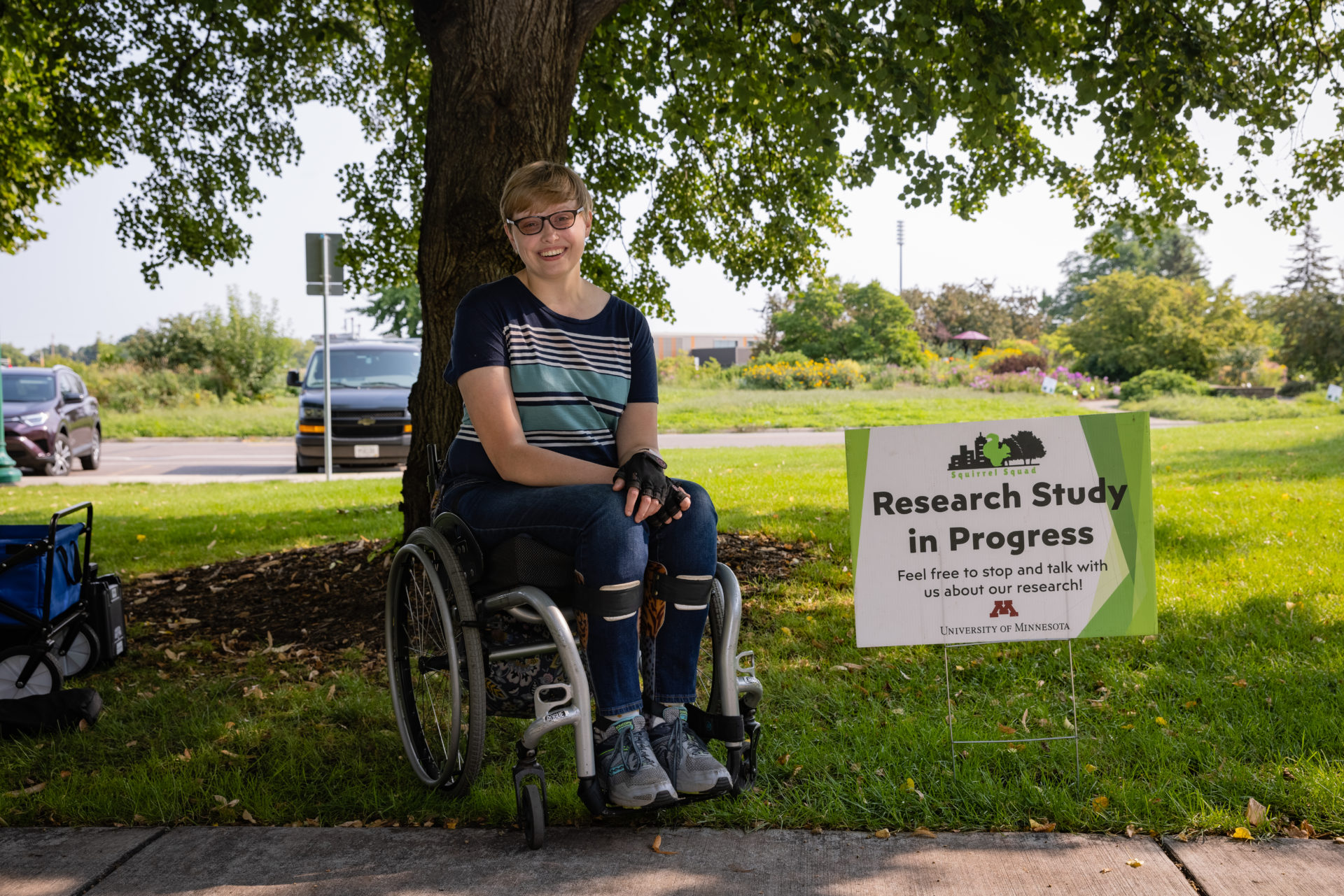 Person in wheelchair smiling directly at camera next to a sign that reads: Research Study in Progress