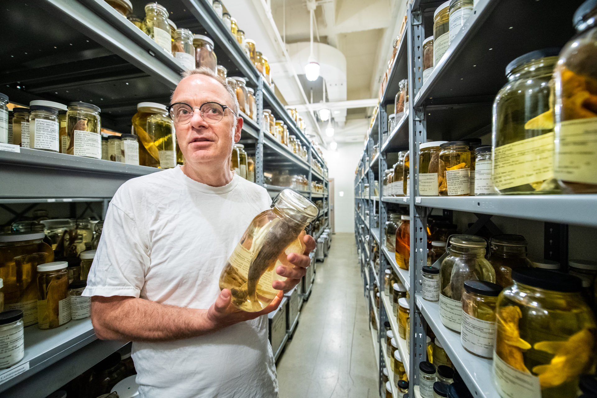 Andrew Simmons standing in a room full of jars with fish specimens