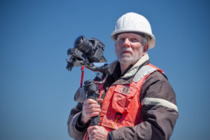 A filmmaker holding a camera and wearing a hardhat