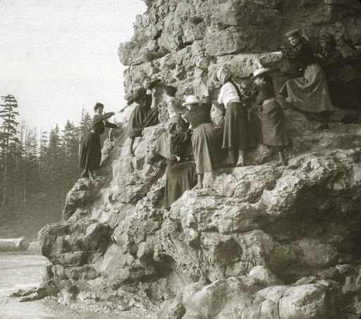 A sepia toned photo of a group of women climbing a rocky shoreline