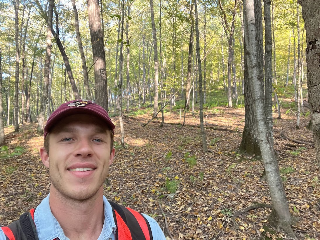 Nick standing in the forest smiling directly at camera.