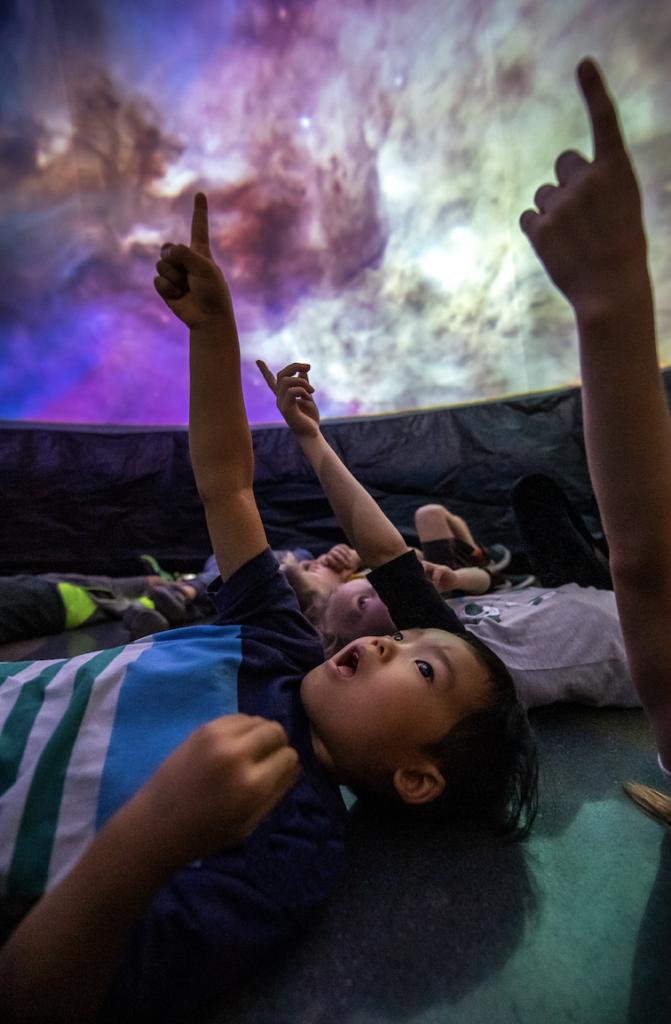 Kids in the ExploraDome pointing up at projections of stars