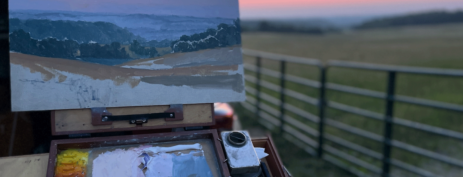 Easel and paint materials set up in front of scenery.
