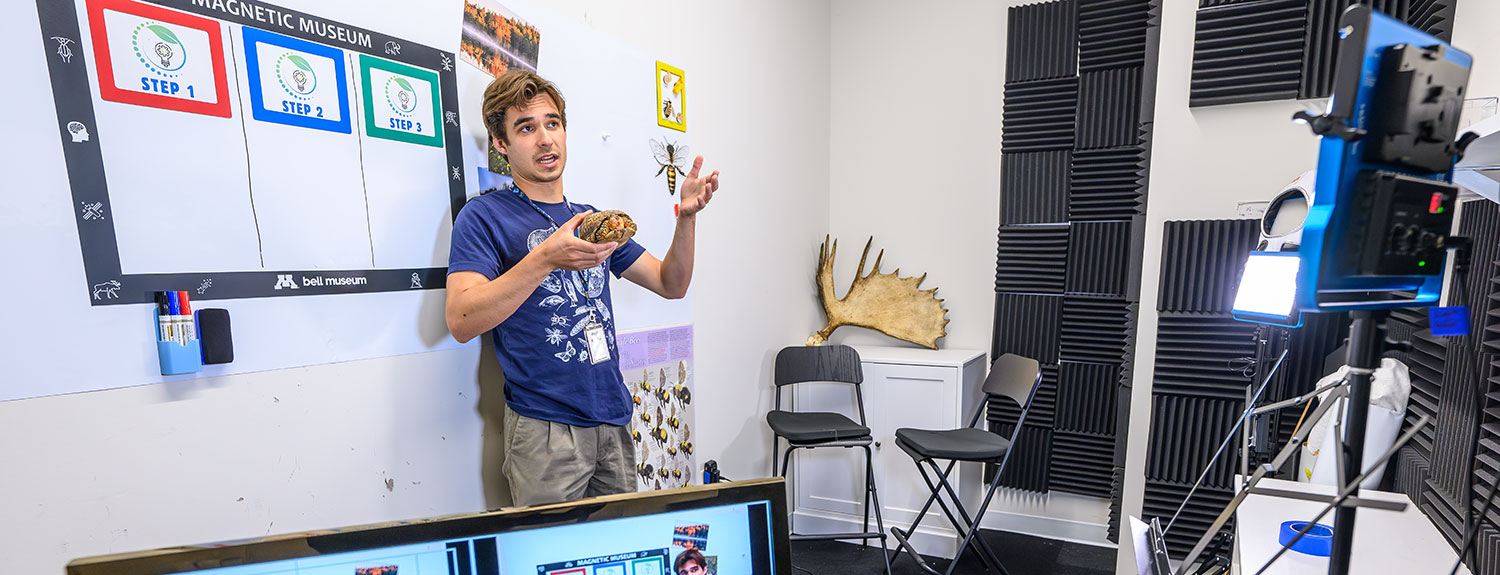 Bell staff member holding specimen to camera with monitors in foreground.